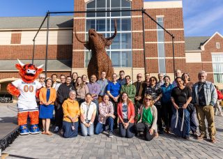 President Suzanne M. Rivera and other campus partners pose in front of the unveiled Coo sculpture, brought to life by figurative sculptor Andy Scott O.B.E.